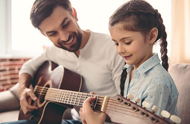 CLASE GUITARRA hombre enseñando a una niña a tocar la guitarra