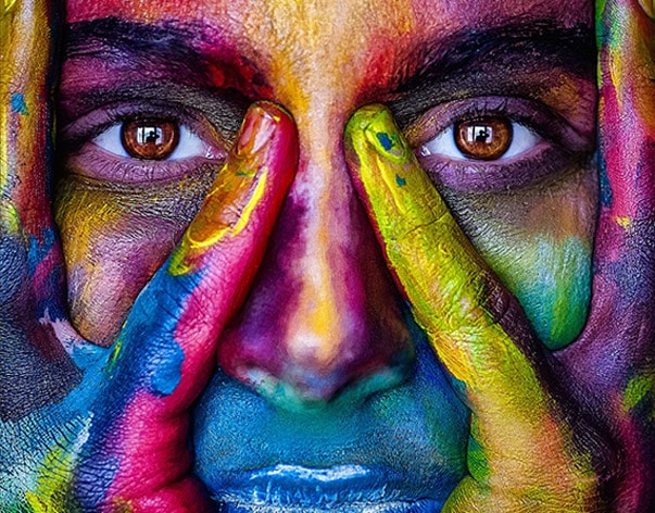 OJOS PINTURA persona con la cara y las manos manchadas de pintura de colores con unos grandes ojos marrones